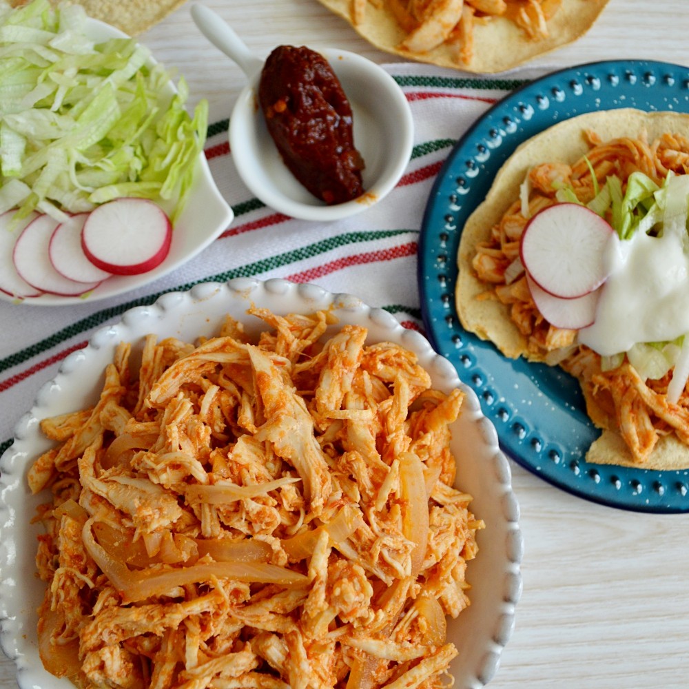 Receta de Tostadas de tinga de pollo tradicional mexicana con aguacate y crema. Cebolla fileteada y pollo deshebrado cocinándose para receta casera.